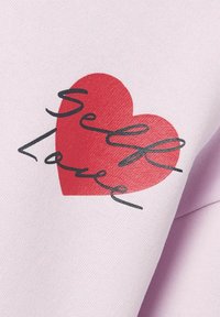 Hellblaues Fabric mit einem großen roten Herzgrafik und dem Text "Selbstliebe" in geschwungener schwarzer Schrift, der im Herzen zentriert ist.