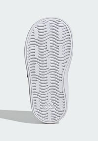 Bílá podrážka tenisky s vlnkovým vzorem a drážkami pro trakci. Obsahuje embosované logo na patě.