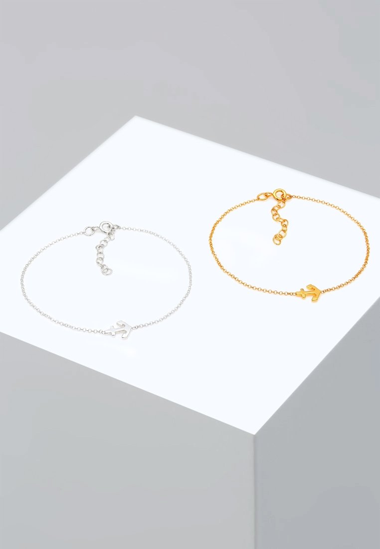 Två armband: ett silver och ett guld. Varje har en delikat kedja med en liten berlock. Kedjorna har justerbara spännen och subtila texturer.