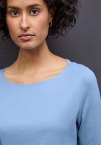 Lichtblauw top met een brede halslijn, lange mouwen en een zachte textuur. Eenvoudig ontwerp zonder zichtbare patronen of versieringen.