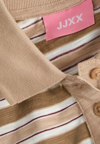 Beige polo-paita, jossa on vaaleanruskeita ja valkoisia raitoja. Varusteena kaulus, kolme beigeä nappia ja vaaleanpunainen etiketti, jossa lukee "JJXX."