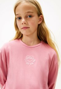 Różowa, długi rękaw t-shirt z okrągłym dekoltem, zdobiony białym haftem w kształcie serca oraz wzorem kwiatowym. Miły w dotyku materiał, luźny krój.