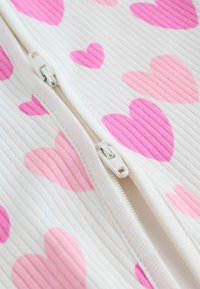 Odzież na zamek błyskawiczny posiada prążkowaną fakturę, białą tkaninę z różnorodnymi różowymi wzorami serduszek, podkreślającymi zabawne i miękkie elementy designu.