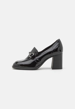 Scarpa con tacco in pelle verniciata nera, con punta arrotondata, dettaglio decorativo con fibbia sulla cinghia e tacco a blocco spesso.