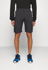 Shorts cargo gris avec devant plat, poches latérales et une taille confortable. Portés avec des chaussures de sport bleues et noires.