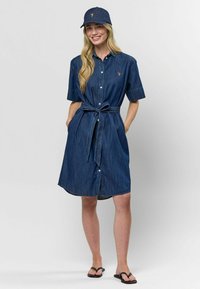 Denimová košeľová šaty v tmavomodrej farbe s krátkymi rukávmi, gombíkovým zapínaním a pásikom v páse. V kombinácii s ladiacou baseballovou čiapkou a čiernymi šľapkami.