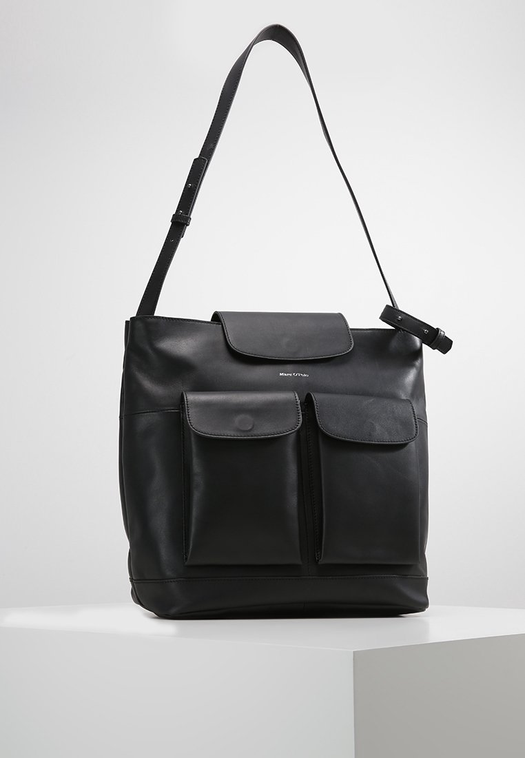 Sac à bandoulière en cuir noir avec deux poches avant à rabat et une bandoulière réglable, présenté sur un socle blanc sur fond uni.