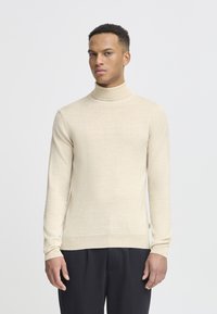 Suéter de cuello alto beige hecho de tela de punto fino. Presenta mangas largas y un diseño ajustado con puños y dobladillo acanalados.