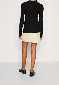 Haut noir à manches longues côtel é associé à une mini-jupe en daim beige, avec un ourlet droit. Le mannequin porte des chaussures vernies noires.