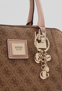 Brączowa torebka wzorzysta z skórzanymi akcentami, złotymi elementami i przywieszką. Posiada wyraźną tabliczkę z logo marki.