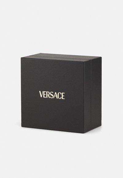 Boîte noire avec une texture mate présentant le logo doré "VERSACE" à l'avant, de forme rectangulaire, au design minimaliste.