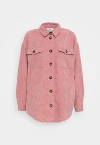 Camicia in corduroy di un morbido rosa, con chiusura a bottoni, due tasche sul petto e bottoni marroni a contrasto. Vestibilità oversize con colletto.