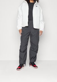 Vit puffjacka med huva, mörkgrå cargobyxor och svarta/röda sneakers. Har en zippered front och textil med struktur samt fickor.