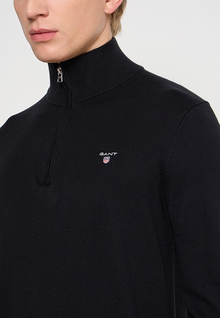 Maglione nero con zip al collo, realizzato in un tessuto a maglia liscia. Presenta un alto colletto e un piccolo logo ricamato sul petto.