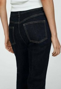 Jeans de mezclilla azul oscuro con un diseño clásico de cinco bolsillos, costuras visibles y una silueta ajustada, mostrando la vista trasera.
