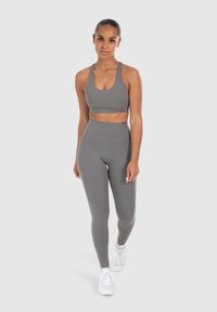 Completo sportivo grigio composto da un reggiseno sportivo aderente e leggings a vita alta, realizzati in tessuto liscio ed elasticizzato. Sneakers bianche completano l'outfit.