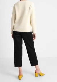 Cremfarbener Rippstrickpullover, schwarze gerade geschnittene Hose, gelbe Absatzmules. Verfügt über übergroße Ärmel und eine lockere Passform. Schlichtes, modernes Design.