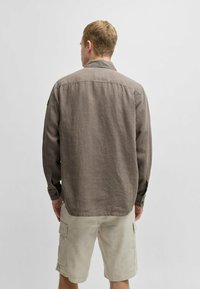  Lichtbruine, lange mouwen, knoopjeshemd met een zachte linnen textuur, voorzien van een kraag en rugpas, gedragen met lichtbeige cargoshorts.