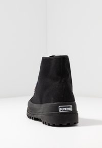 Czarne wysokie trampki materiałowe z wytrzymałą podeszwą, widok od tyłu, z logo "Superga" na pięcie.