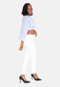 Blusa accorciata di colore azzurro chiaro con maniche a palloncino, abbinata a jeans bianchi attillati e tacchi alti neri a punta. Texture del tessuto liscia.