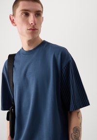 Camiseta azul marino de manga corta acanalada, con cuello redondo y logo bordado "BOSS" en el pecho. Textura de tela suave.