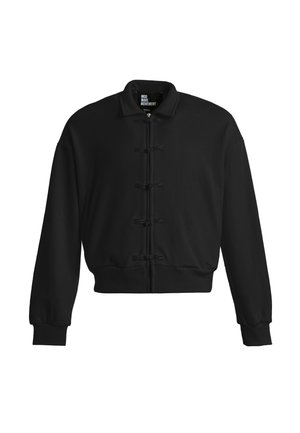 Chaqueta bomber negra con cremallera frontal y cinco cierres decorativos en forma de nudos, puños y cinturilla acanalados, y un pequeño cuello de pie.