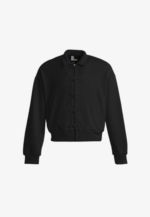 Chaqueta bomber negra con cremallera frontal y cinco cierres decorativos en forma de nudos, puños y cinturilla acanalados, y un pequeño cuello de pie.