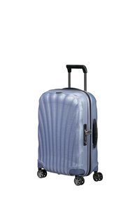 Hard-shell carry-on suitcase in light blue with ridged texture, black telescopic handle, four spinner wheels, and combination lock.