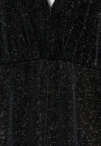 Schwarzer Samtstoff mit dichten, kleinen silbernen Glitzertropfen, die ein funkelndes und strukturiertes Muster erzeugen, das plissierte Details zeigt.