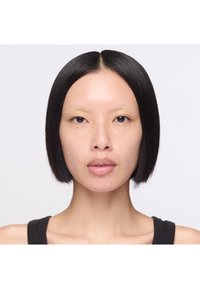Porträtt av en person med rakt, glansigt svart hår som är stylat i en bob. Huden är slät och lätt texturerad, med subtila naturliga toner.
