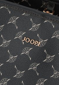 Material texturizado negro con un patrón abstracto blanco repetido. Logotipo en tono dorado "JOOP!" acentuado y exhibido de manera prominente.