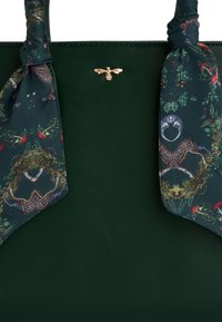 Zelená kožená taška s vzorovanou šatkou naviazanou na rúčkach. Šatka zobrazuje prírodný motív so zvieratami a rastlinami. Na prednej strane sa nachádza zlaté logo včely.