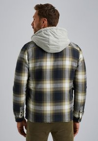 Chaqueta de cuadros con un patrón en azul marino, gris y amarillo, con capucha gris y detalles de botones en los laterales, hecha de una tela suave y texturizada.