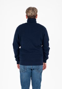 Maglione a coste di colore blu navy con colletto alto, indossato sopra jeans azzurri. La parte posteriore presenta un design aderente e un tessuto testurizzato.