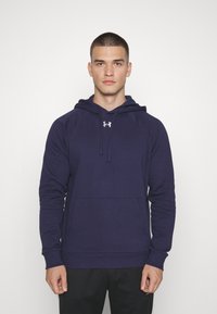 Marineblauwe hoodie, gemaakt van zachte stof, heeft een voorzak en een Under Armour-logo op de borst. Strakke pasvorm met ribgebreide manchetten.