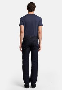 Marinblå t-shirt med kort ärm som bärs tillsammans med mörk denimjeans. Jeansen har bakfickor och en rak ben design. Svarta skor.