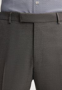Gray trousers made of textured fabric featuring a flat front, belt loops, and a smooth waistband, worn with a patterned shirt.