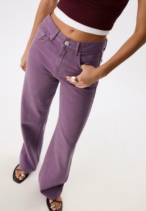 Lila weite Denim-Jeans mit Fronttaschen, Knopfverschluss und glatter Textur. Kombiniert mit braunen Sandalen.