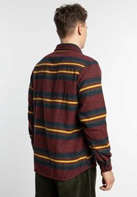 Camisa de franela color burdeos con rayas horizontales en verde oscuro y amarillo. Presenta un collar, puños con botón y un dobladillo redondeado.