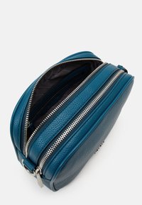 Blågrön läderväska med texturerad yta, två dragkedjeförsedda fack, silverdetaljer och svart innerfodring. Stabil, strukturerad form.