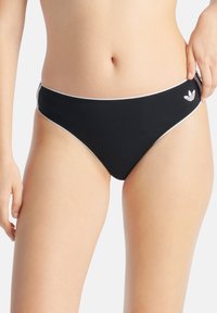 Svart bikiniunderdel med låg midja, med vit kantband längs kanterna och en liten vit Adidas-logga på höften.