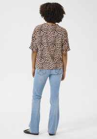 Blusa a maniche corte con stampa leopardata in beige e nero, abbinata a jeans svasati di colore blu chiaro. L'outfit presenta una vestibilità comoda e un tessuto morbido.