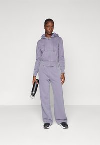 Purple hoodie with a zipper, drawstring, and logo, paired with matching sweatpants. The outfit has a relaxed fit and soft fabric texture.