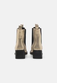 Bottes cheville noires et dorées avec une finition métallique texturée, talons carrés et panneaux latéraux élastiques. Dotées de languettes à l'arrière.