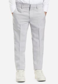 Pantaloni grigi chiari in tessuto morbido, con vestibilità sagomata, due tasche laterali e una vestibilità frontale piatta. Indossati con sneakers bianche.