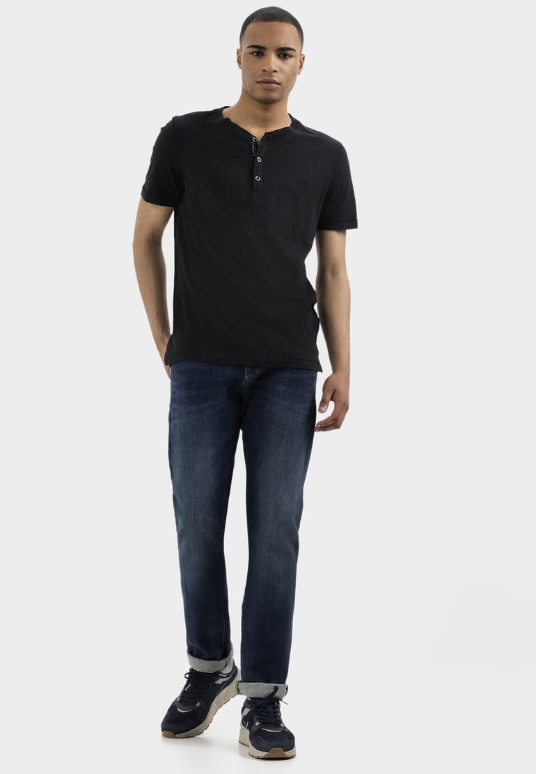 Chandail henley noir à manches courtes avec trois boutons, associé à un jean bleu foncé et des baskets noires avec des accents clairs. Coupe et design décontractés.