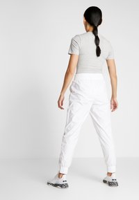 Šedé tričko s krátkými rukávy, bílé tepláky s elastickým pasem, žebrované manžety a bílé tenisky s černobílým vzorem na podrážce.