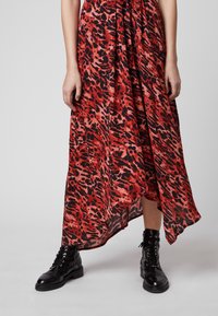 Abito maxi in stampa animale rossa e nera, caratterizzato da una silhouette fluida e orlo asimmetrico. Abbinato a stivaletti neri con lacci alla caviglia.
