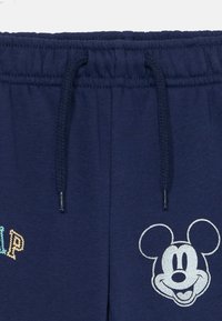 Námorníckomodré tepláky s elastickým pásom, sťahovacou šnúrkou, multicolor textom "Jump" a potlačou usmievajúcej sa hlavy Mickey Mouse v bielej farbe.