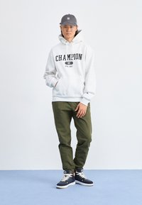 Sivá bavlnená mikina s logom "CHAMPION", olivové nohavice, námornícke vysoké tenisky s bielymi akcentmi a sivá šiltovka. Neformálny outfit.